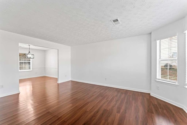 empty room with dark wood finished floors, visible vents, a textured ceiling, and baseboards