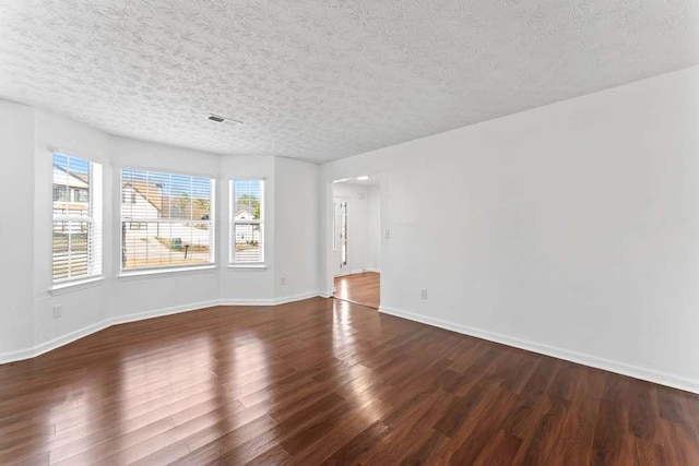 unfurnished room featuring visible vents, a textured ceiling, baseboards, and wood finished floors