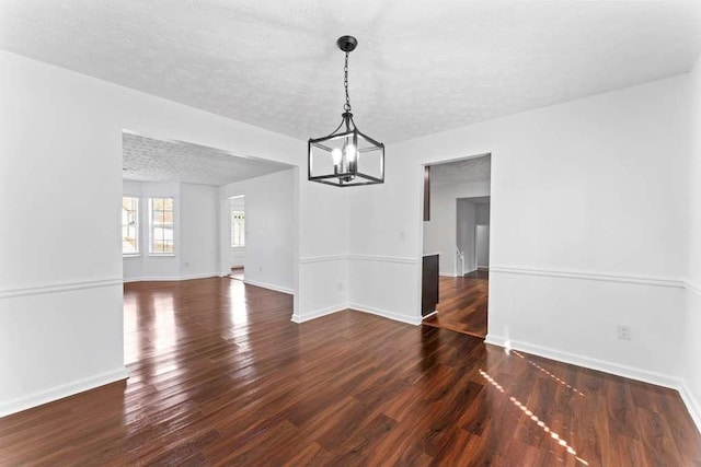 unfurnished dining area featuring baseboards, a textured ceiling, an inviting chandelier, and wood finished floors