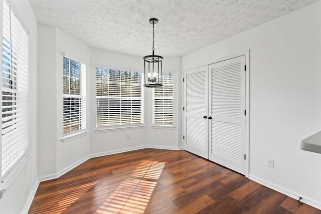 unfurnished dining area with a notable chandelier, wood finished floors, and baseboards