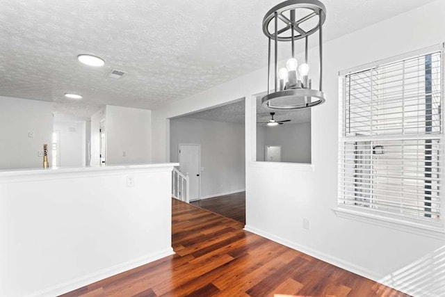 interior space featuring a ceiling fan, visible vents, baseboards, dark wood-type flooring, and a textured ceiling