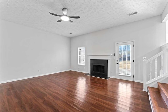 unfurnished living room featuring visible vents, a fireplace with raised hearth, ceiling fan, stairway, and wood finished floors