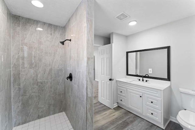 full bathroom featuring visible vents, toilet, wood finished floors, tiled shower, and vanity