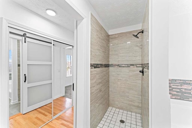 full bath featuring a textured ceiling, wood finished floors, and tiled shower