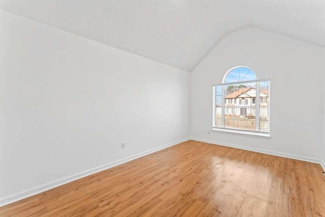 empty room with lofted ceiling, light wood-style flooring, and baseboards