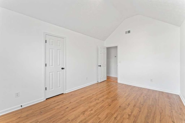 empty room with light wood finished floors, visible vents, high vaulted ceiling, and baseboards