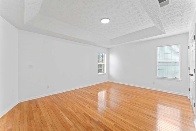 empty room with baseboards, a raised ceiling, a textured ceiling, and light wood-style flooring