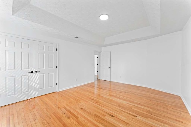 spare room with a tray ceiling, baseboards, a textured ceiling, and light wood finished floors