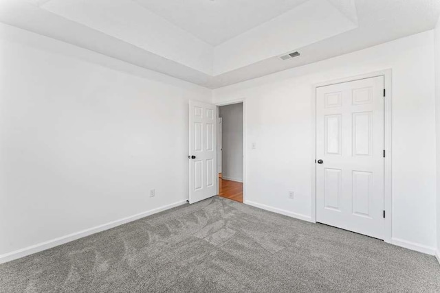 unfurnished bedroom with a tray ceiling, carpet flooring, visible vents, and baseboards