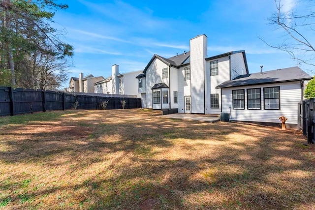 rear view of house with a patio, central AC unit, a yard, a fenced backyard, and a chimney