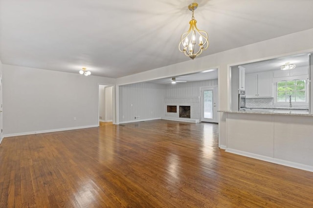 256 Teresa Ln, Loganville, GA 30052 - unfurnished living room with a chandelier, wood finished floors, a ceiling fan, and a brick fireplace