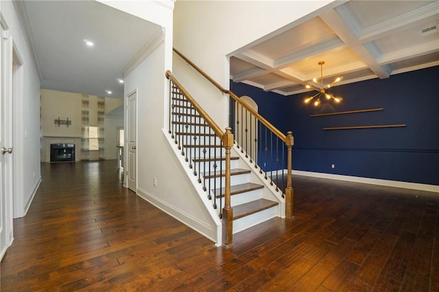 staircase with wood-type flooring, coffered ceiling, beam ceiling, a notable chandelier, and ornamental molding