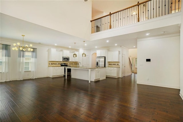 unfurnished living room with a notable chandelier, dark hardwood / wood-style floors, a towering ceiling, crown molding, and sink