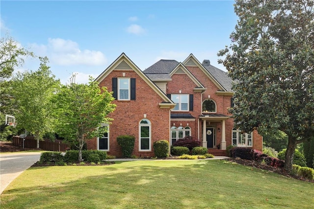 view of front of property featuring fence, a chimney, a front lawn, and brick siding