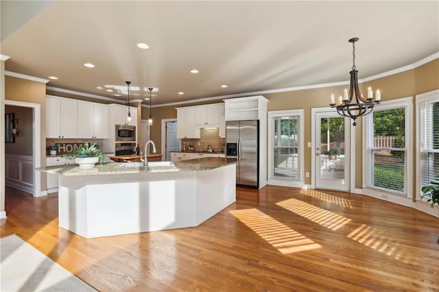 kitchen with a notable chandelier, stainless steel appliances, a large island, decorative backsplash, and ornamental molding