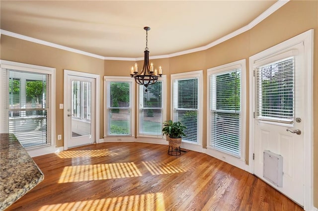 doorway featuring a healthy amount of sunlight, ornamental molding, light wood-type flooring, and a chandelier