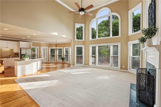 unfurnished living room featuring crown molding, a towering ceiling, a fireplace, baseboards, and ceiling fan with notable chandelier