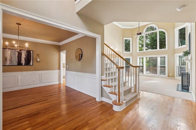 interior space featuring ornamental molding, wainscoting, wood finished floors, a decorative wall, and ceiling fan with notable chandelier