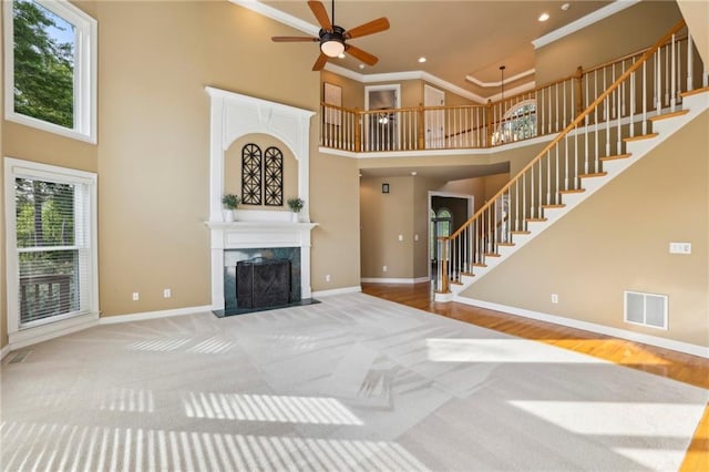 unfurnished living room with carpet, stairs, a ceiling fan, a towering ceiling, and visible vents