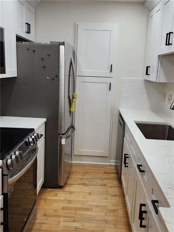 kitchen featuring light stone counters, appliances with stainless steel finishes, a sink, and white cabinetry