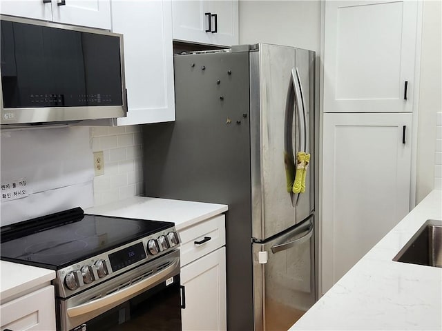 kitchen with light stone counters, white cabinetry, stainless steel appliances, and backsplash