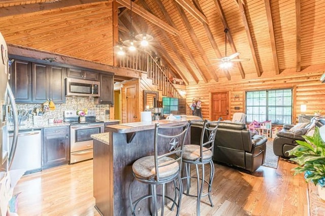 kitchen with beam ceiling, rustic walls, light hardwood / wood-style floors, wood ceiling, and appliances with stainless steel finishes