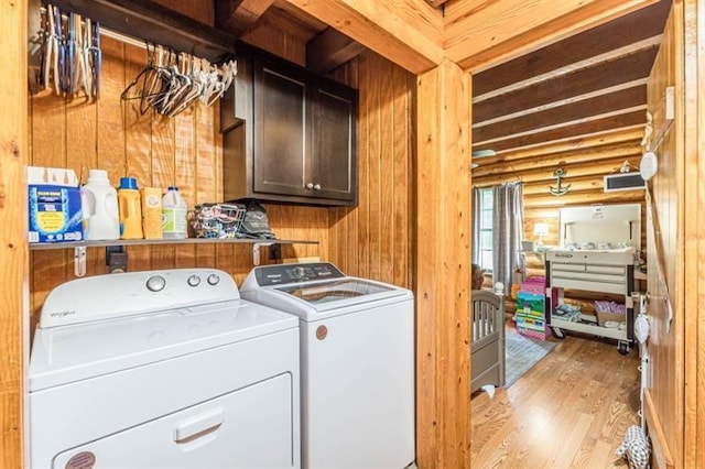 washroom featuring log walls, cabinets, independent washer and dryer, light hardwood / wood-style floors, and wooden walls