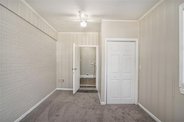 unfurnished bedroom featuring ceiling fan, brick wall, carpet floors, ornamental molding, and a closet