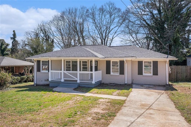 view of front of home with brick siding, a porch, a shingled roof, a front yard, and fence