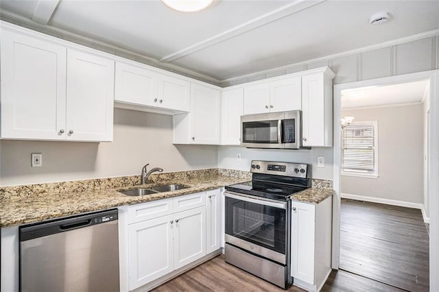 kitchen featuring stainless steel appliances, wood finished floors, white cabinets, a sink, and light stone countertops