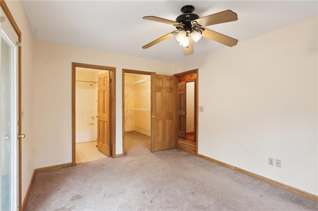 unfurnished bedroom with baseboards, a walk in closet, a closet, and light colored carpet