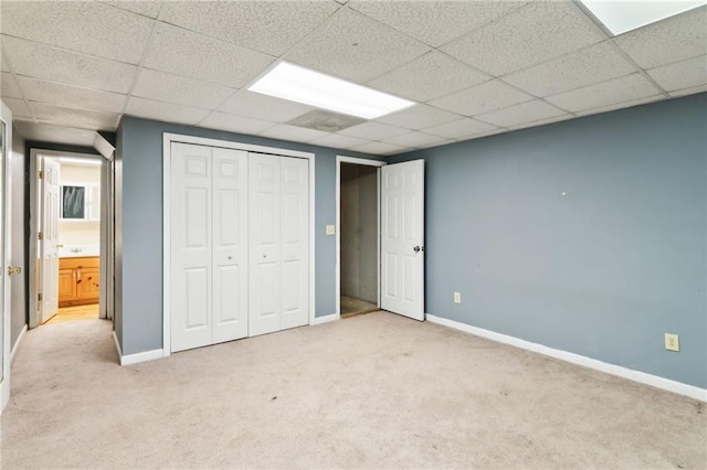 unfurnished bedroom with a paneled ceiling, a closet, light colored carpet, and baseboards