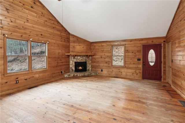 unfurnished living room featuring a fireplace, light hardwood / wood-style flooring, high vaulted ceiling, and wood walls