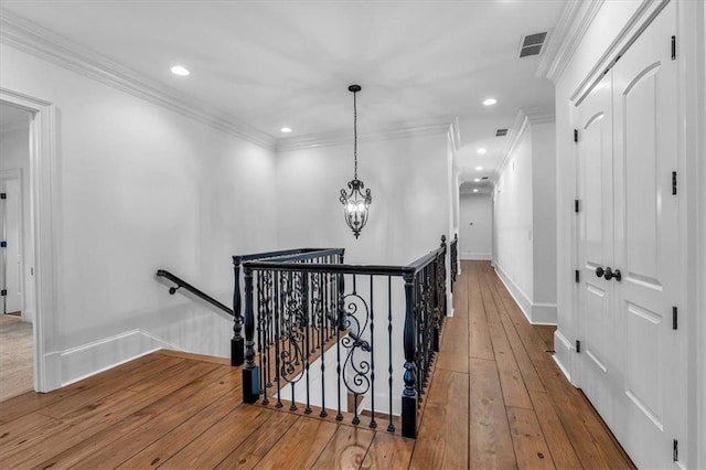 hallway featuring an upstairs landing, visible vents, baseboards, ornamental molding, and wood-type flooring