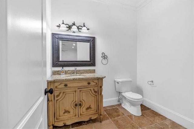 bathroom featuring baseboards, ornamental molding, toilet, vanity, and stone tile floors