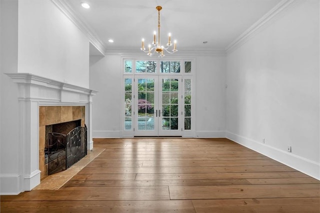 unfurnished living room featuring wood-type flooring, ornamental molding, baseboards, a chandelier, and a tile fireplace