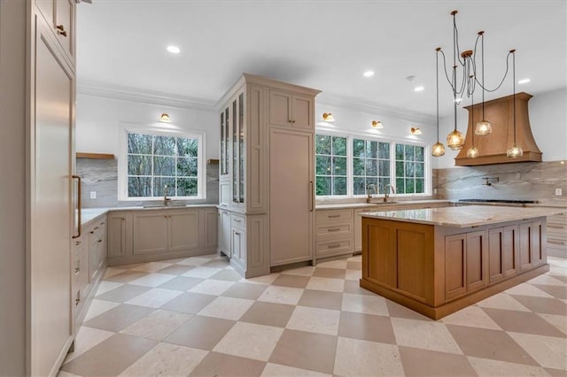 kitchen featuring premium range hood, ornamental molding, a sink, glass insert cabinets, and light floors