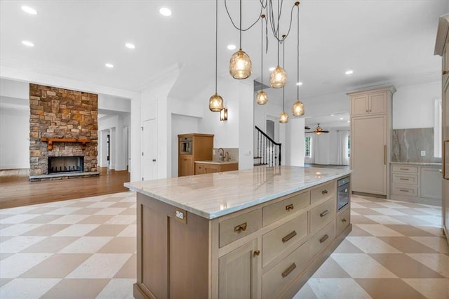 kitchen featuring light stone countertops, a kitchen island, a stone fireplace, light floors, and a sink