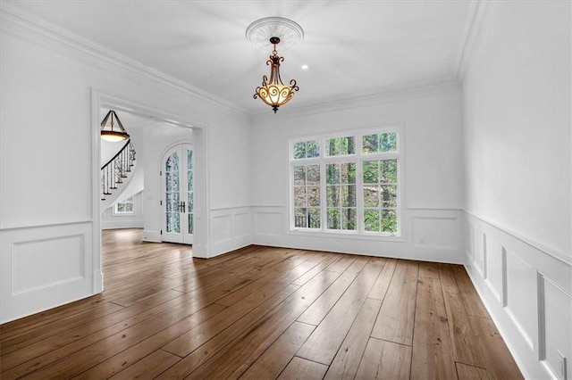 unfurnished dining area with stairs, hardwood / wood-style floors, ornamental molding, a chandelier, and a decorative wall