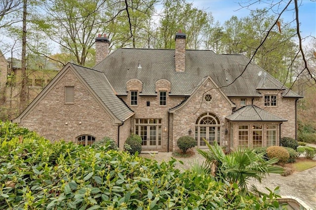 rear view of property with brick siding, a chimney, and french doors