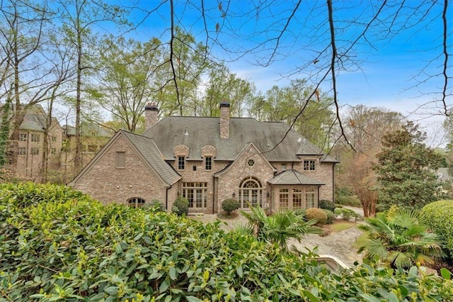 back of property featuring stone siding, driveway, and a chimney