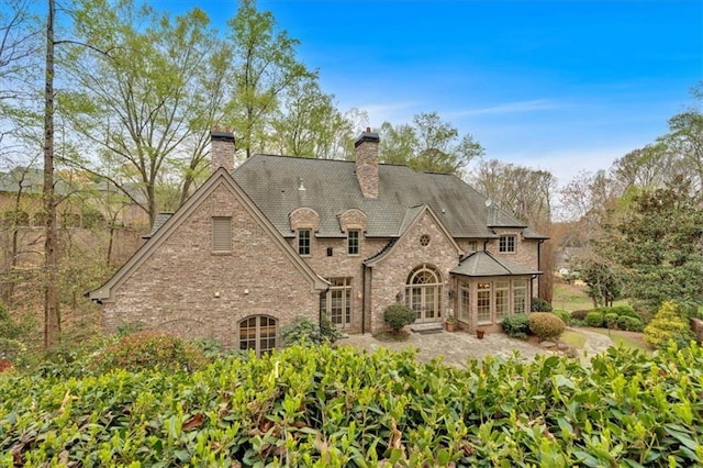 rear view of property with brick siding, a chimney, and french doors