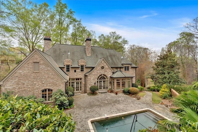 back of house featuring stone siding, french doors, a chimney, a patio, and an outdoor pool