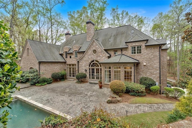 rear view of property with stone siding, a patio, a chimney, brick siding, and french doors