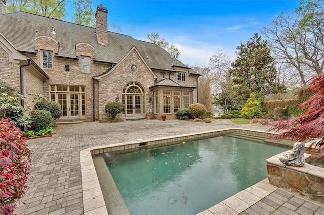 rear view of property featuring stone siding, a chimney, french doors, and a patio area