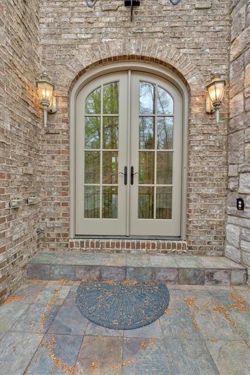 doorway to property featuring brick siding, stone siding, and french doors