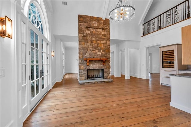 unfurnished living room featuring high vaulted ceiling, visible vents, light wood-style flooring, a chandelier, and a fireplace