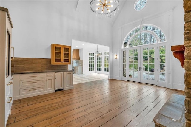interior space featuring a notable chandelier, french doors, light wood-style flooring, baseboards, and a towering ceiling