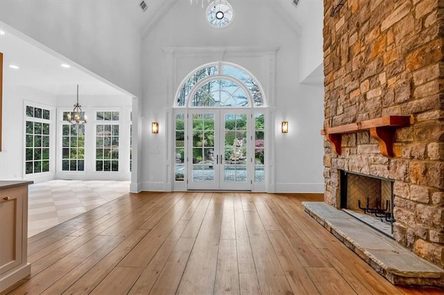 interior space with french doors, light wood finished floors, a fireplace, a high ceiling, and an inviting chandelier