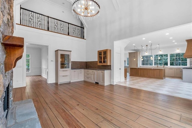 unfurnished living room featuring a stone fireplace, light wood-type flooring, a towering ceiling, and a chandelier